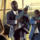 Artwork shows three masked men running out of a bank carrying SMGs.